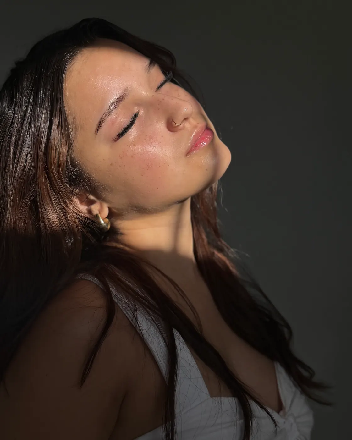 A client with glowing skin, eyes closed, face lifted toward warm light