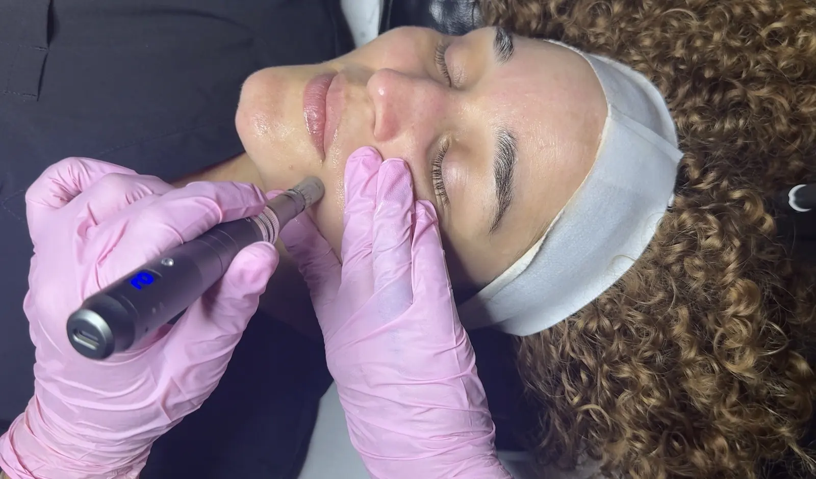 An esthetician in pink gloves treating a client's cheek with a handheld skin device
